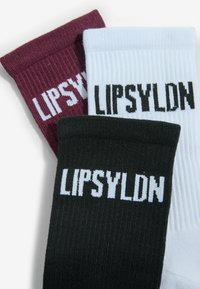 Trois chaussettes côtelées en bordeaux, blanc et noir, chacune avec le texte « LIPSYLDN » près du bord côte dans des couleurs contrastantes.