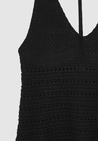 Haut sans manches au crochet noir avec décolleté en V et motif en tricot texturé, mettant en valeur un travail de points détaillé sur la zone du haut du torse.