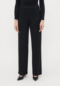 Zwarte wijde broek met een gestructureerd verticaal streepjespatroon. Beschikt over een elastische tailleband en gladde stof. Gecombineerd met zwarte puntige hakken.