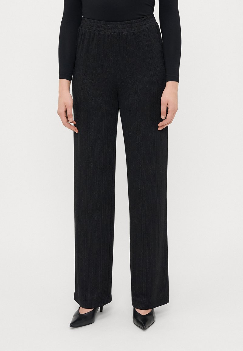 Zwarte wijde broek met een gestructureerd verticaal streepjespatroon. Beschikt over een elastische tailleband en gladde stof. Gecombineerd met zwarte puntige hakken.