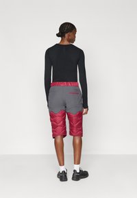 Σορτς με επένδυση σε γκρι βάση και μπορντό επενδύσεις, με φαρδιά ελαστική μέση. Ένα μαύρο μπλουζάκι με μακριά μανίκια είναι επίσης ορατό.