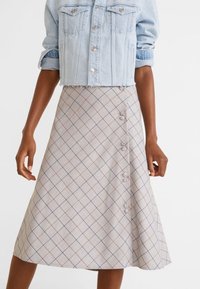 Une veste en denim bleu clair portée sur une jupe à carreaux gris. La jupe présente une fermeture boutonnée à l'avant avec de petits boutons clairs et une coupe évasée.