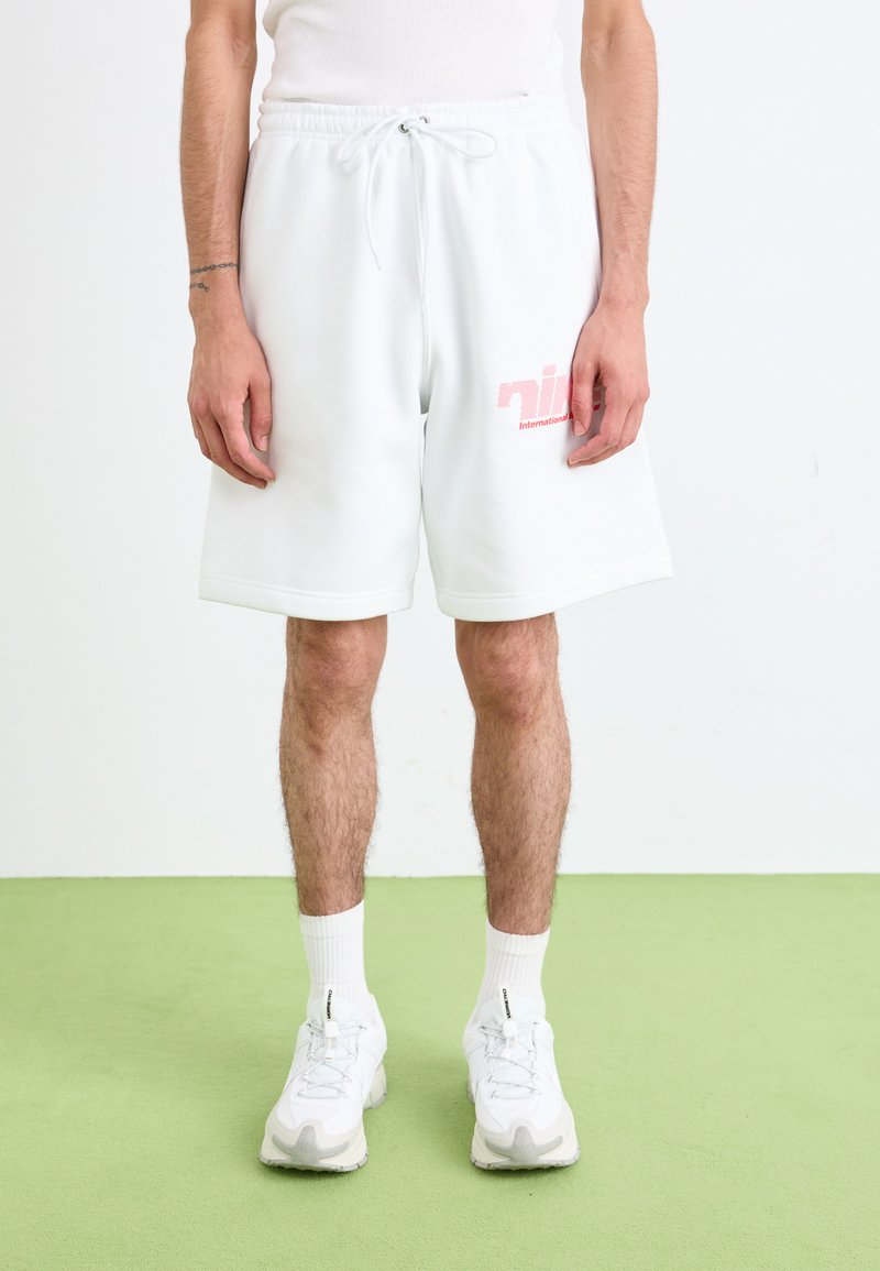 Hvide bomuldsshorts med elastisk talje og snor. Har et pink logo på venstre ben. Bæres med hvide sneakers og sokker.