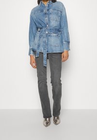 Ljusblå jeansskjorta med bälte i midjan, knäppt fram och bröstficka. Kombineras med gråa figurnära jeans och metalliska spetsiga skor.