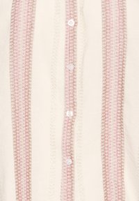 Blouse en tissu léger présentant des rayures verticales rose et beige, avec cinq boutons blancs sur le devant et des accents texturés partout.