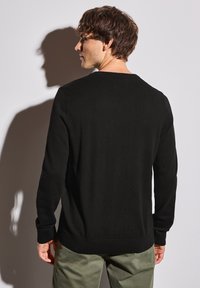 Svart stickad tröja med långa ärmar och rundad halsringning. Slät textur, åtsittande manschetter och en fåll som sitter precis under midjan.