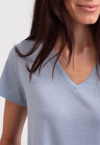 Světle modré v-výstřih tričko vyrobené z měkké, strukturované látky s krátkými rukávy. Výstřih a okraje rukávů jsou pečlivě zpracovány.
