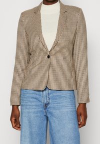 Brązowo-kremowa kraciasta marynarka zapinana na jeden guzik, dopasowana, z długimi rękawami. W połączeniu z jasnoniebieskimi, wysokim stanem dżinsami.