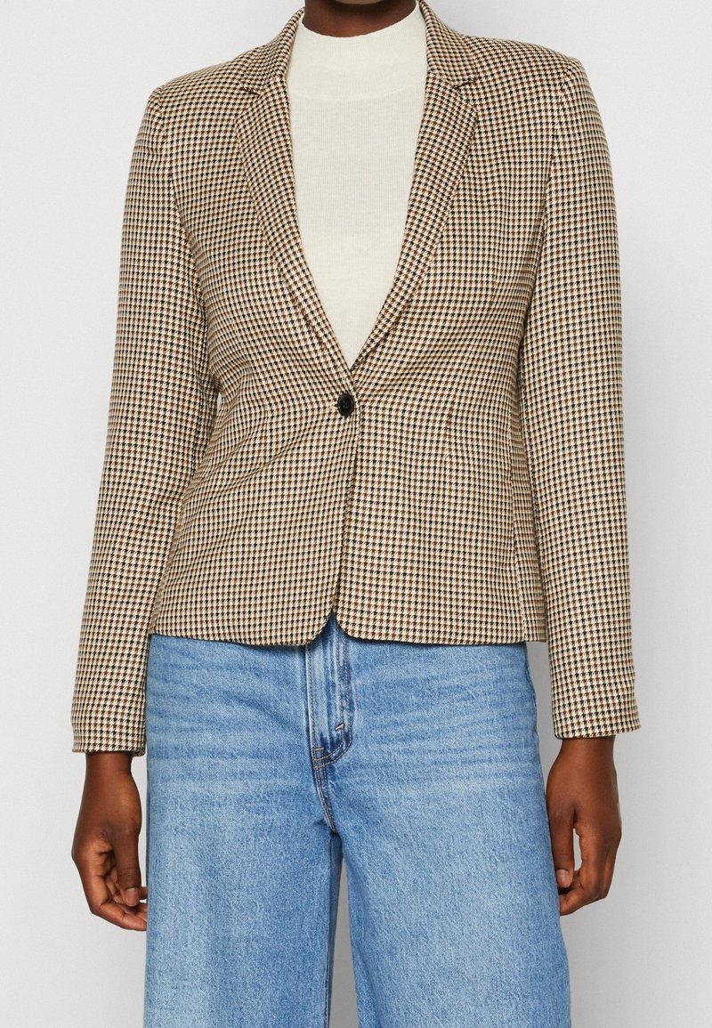 Brązowo-kremowa kraciasta marynarka zapinana na jeden guzik, dopasowana, z długimi rękawami. W połączeniu z jasnoniebieskimi, wysokim stanem dżinsami.