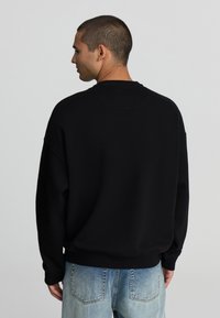 Felpa nera con una vestibilità comoda, scollatura rotonda e spalle scese. Tessuto morbido con polsini e orlo a costine, abbinata a jeans blu chiaro.