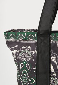 Tote bag featuring a black patterned fabric with green and white floral motifs, complemented by sturdy black straps and a structured shape.
