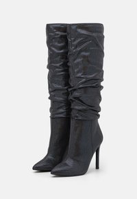 Botas de tornozelo pretas de salto alto com um design solto, feitas de material brilhante. Apresentam bicos pontiagudos e um acabamento texturizado elegante.
