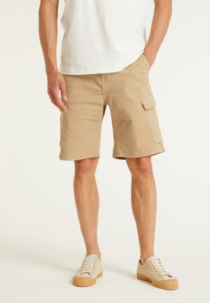 Shorts cargo khaki à coupe droite, avec plusieurs poches latérales et une texture en coton lisse, complétés par des baskets beiges à lacets.