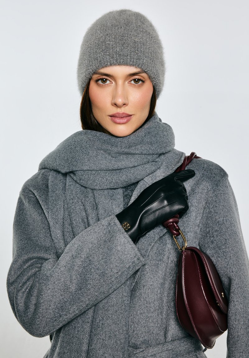 Šedý vlněný kabát se sladěnou šálou, černé kožené rukavice a vínově červená kabelka. Šála má texturovaný vzhled a kabelka je zaobleného tvaru.