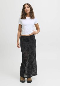 Gonna lunga nera in tessuto trasparente con motivo floreale, abbinata a una t-shirt bianca e stivaletti marroni.