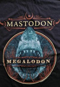 Czarna koszulka z graficznym wzorem dużego rekina megalodona, otoczona czerwonymi i niebieskimi okrągłymi akcentami oraz słowem "MASTODON."