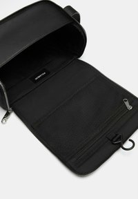 Borsa in pelle nera con apertura a zip, dotata di una tasca in rete e di un compartimento con zip all'interno. Etichetta PULL&BEAR visibile all'interno.