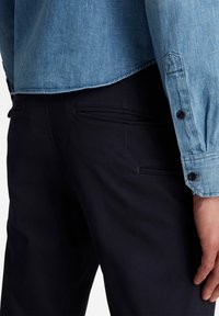 Ljusblå denimskjorta med långa ärmar och svarta knappar, i kombination med m örkblå byxor med horisontella fickor.