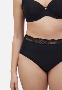 Bragas negras de talle alto con una cinturilla de encaje. Textura suave y diseño ajustado, con detalles de encaje en el borde superior.