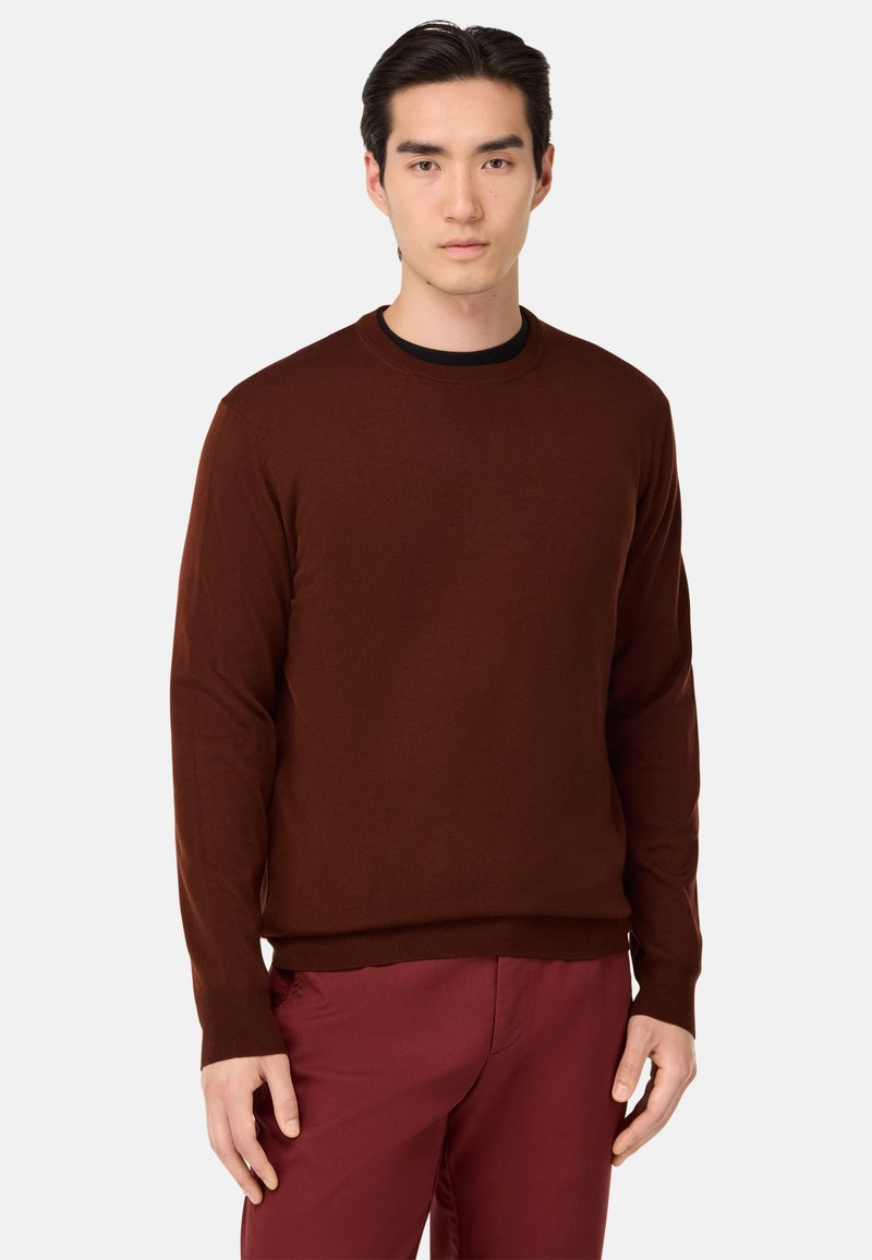 Rjav pleten sveter z okroglim izrezom in dolgimi rokavi, z gladko teksturo in rebrastimi manšetami, v kombinaciji s svojim maroon hlačami.