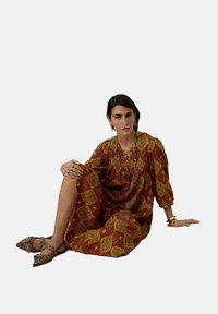 Robe rouge à motifs géométriques, à manches trois-quarts et à coupe décontractée. Accessoirisée avec des colliers superposés et des bracelets.