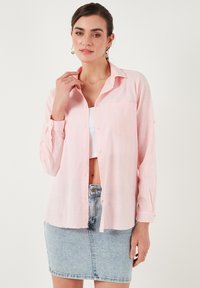 Light pink button-up shirt with a relaxed fit, single chest pocket, and long sleeves, paired with a denim mini skirt. Textured fabric.