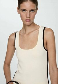 Beige sleeveless top with a square neckline, contrasting black side accents, and a ribbed texture. Simple design without additional embellishments.