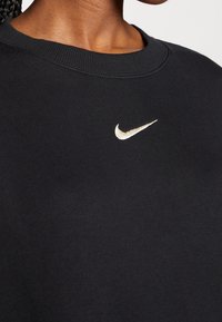Sudadera negra con cuello redondo y un logo de Nike bordado en dorado en el pecho. Tejido suave con una textura lisa.
