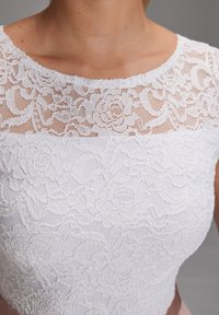 Biała koronkowa góra z floralnym wzorem, z okrągłym dekoltem i przezroczystą warstwą. Gładka dolna część w jednolitym białym materiale.