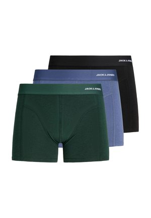 Ung voksen mand med kort blondt hår iført mørkegrønne boxershorts stående mod en ensfarvet lys baggrund, vendt mod fronten med neutralt udtryk.
