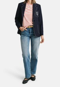 Navy blazer with white stitching and a patch pocket, paired with a red-striped t-shirt and light blue jeans, completed with black shoes.