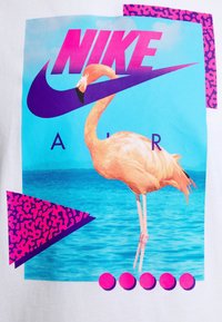 Nike Air grafisk t-shirt med vit bas, prydd med en rosa flamingo, blå vattenfond, djärva rosa och lila geometriska former samt runda accenter.