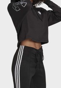 Mustat lyhyet hupparit, joissa on sileä rakenne ja valkoinen logo; yhdistetty mustiin verkkareihin, joissa on kolme valkoista pystysuoraa raitaa kummallakin puolella.