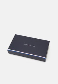Scatola regalo Tommy Hilfiger, forma rettangolare, blu navy scuro con una striscia di accento bianca e rossa lungo il bordo, logo centrato sulla parte superiore.