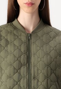 Veste bomber matelassée vert olive avec fermeture éclair à l'avant, arborant un motif floral et un col côtelé. Texture douce et design rembourré.