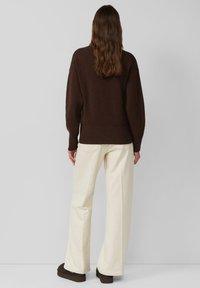 Brauner Pullover mit geripptem Saum, kombiniert mit cremefarbenen Hosen mit weitem Bein und braunen Schuhen. Weiche Textur, entspannte Passform und minimalistische Details.