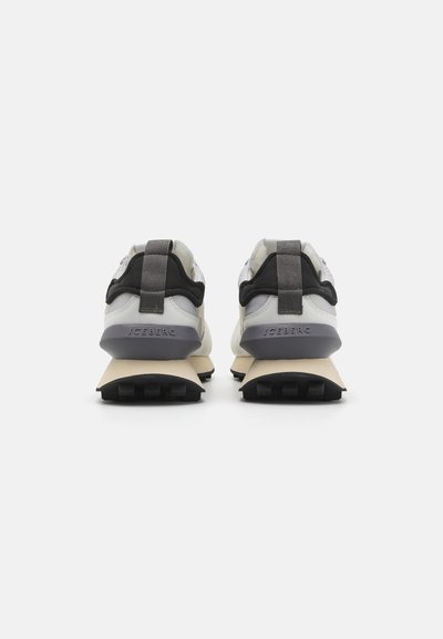 Sneakers featuring a gray and black textile upper, beige midsole, and textured black outsole. Striped heel tab and branded detail on the sole.
