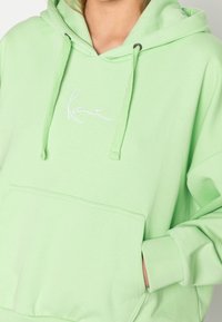 Felpa verde chiaro con tasca a marsupio, cordoncini e logo ricamato bianco. Realizzata in morbido tessuto di cotone con polsini a costine.