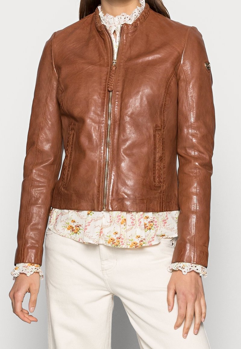 Hnědá kožená bunda s přiléhavým střihem, zapínáním na zip a dvěma předními kapsami. Disponuje hladkým povrchem a ozdobnými švy.