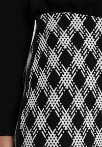 Tela de patrón en blanco y negro con un diseño de diamantes, superficie texturizada y una sección negra lisa en la parte superior.