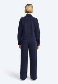 Navy blue, soft fabric outfit featuring a fitted jacket with long sleeves and matching wide-leg trousers. Simple design, no patterns or accents.