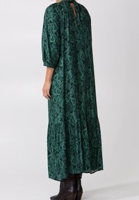 Vestido maxi de color verde con un diseño estampado, espalda con abertura en forma de lágrima, mangas de tres cuartos con volantes y falda de capas. Tejido suave con una silueta fluida.