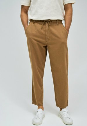 Pantalones de algodón ligeros y en tono marrón con cintura elástica y cordón. Cuentan con dos bolsillos laterales y un corte relajado, combinados con zapatillas blancas.