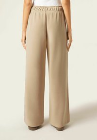 Ljust beige vida byxor med elastisk midja och slät textur, med en lös passform och rak silhuett.