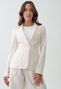 Quilted pastel pink blazer with a shawl collar, single-button closure, and textured shell pattern, paired with matching pants.