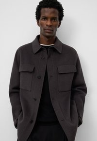 Ciemnoszara kurtka z mieszanki wełny z kołnierzowym wykończeniem, posiadająca dwie kieszenie na piersi, zapięcie na guziki oraz gładką teksturę.