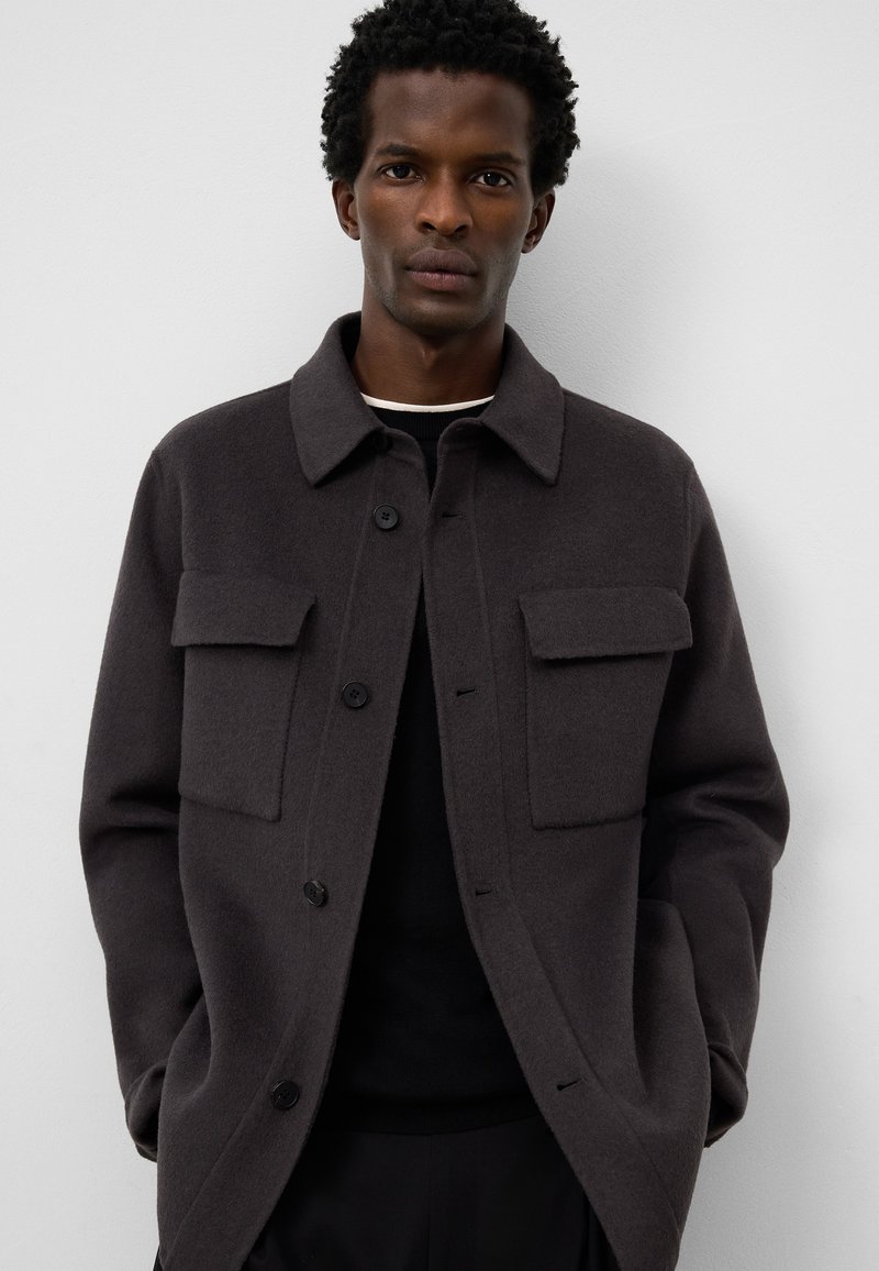 Ciemnoszara kurtka z mieszanki wełny z kołnierzowym wykończeniem, posiadająca dwie kieszenie na piersi, zapięcie na guziki oraz gładką teksturę.