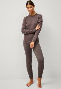 Aangesloten bruine lange mouwen top en bijpassende legging van zacht, soepel materiaal. Bevat subtiel logo detail op de mouw.
