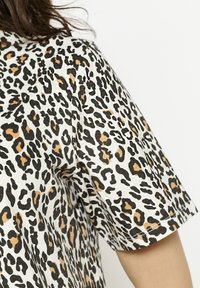 Kurzärmeliges Oberteil aus leichtem Material mit weißem Grund und schwarzem sowie beigem Leopardenmuster, glatte Textur mit umgeschlagenem Saum.