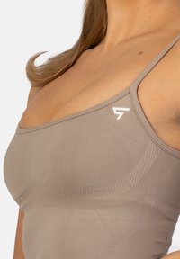 Lichtbruine sportbeha met verstelbare spaghetti bandjes, geribbelde textuur, subtiele logo-detail en een naadloos ontwerp voor comfort.